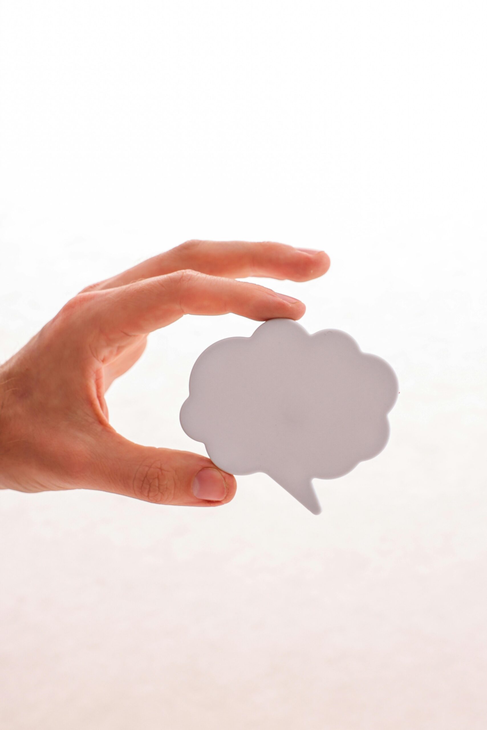 A hand holding a cloud-shaped speech bubble cutout on a neutral background.